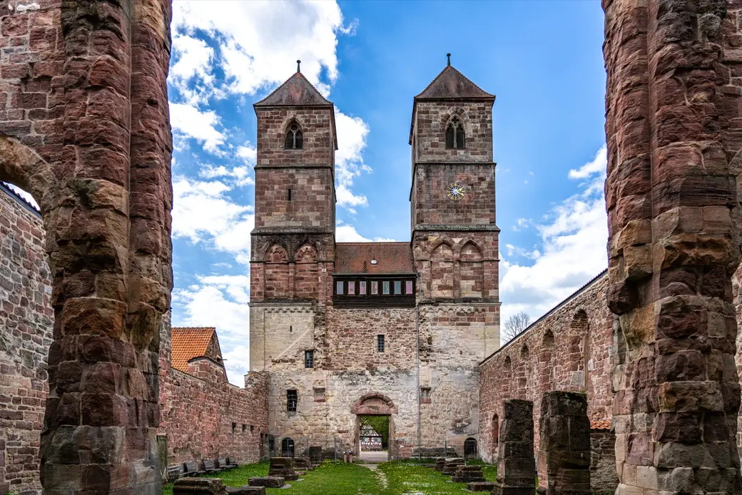 Die beiden Sandsteintürme der Klosterkirche Veßra, gesehen aus dem grasbewachsenen Inneren der Kirchenruine zwischen zwei Pfeilern hindurch.